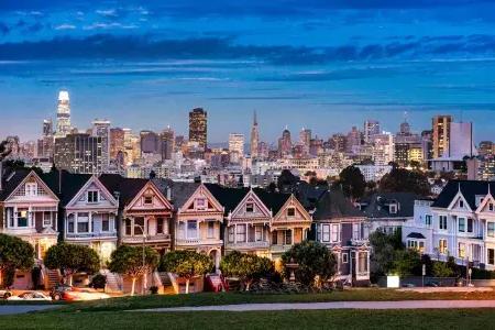 The famous Painted Ladies of Alamo Square pictured before The San Francisco skyline at twilight.