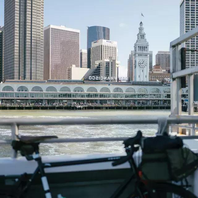 Bicicleta encostada em um trilho 和 o Ferry Building ao fundo.